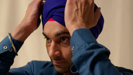 Studio-Shot-Of-Sikh-Man-Wearing-And-Checking-Turban-Against-Plain-Background